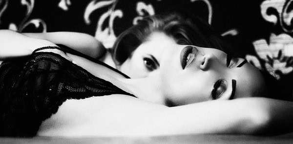Erotic black and white image of two women lying on bed.