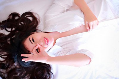 Young Asian girl lying on bed giving OK sign