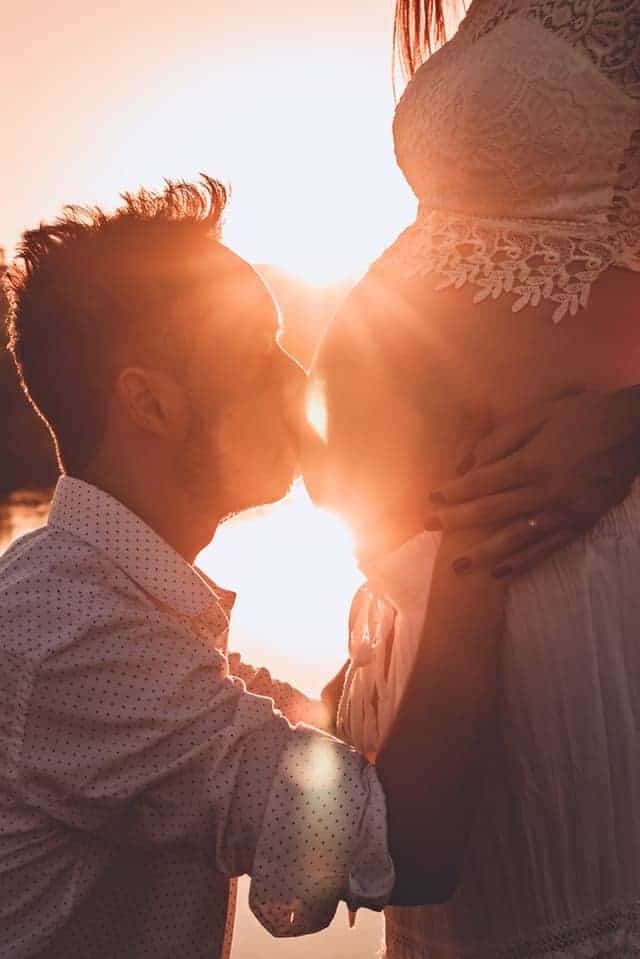 Man kissing pregnant wife's belly at sunset