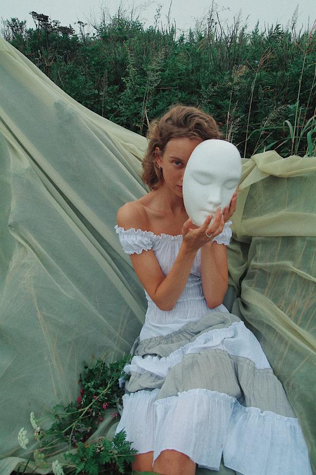 Woman sitting holding a white mask next to her face